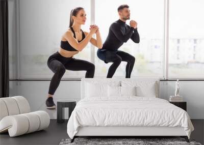 Deep squat. Fitness couple in sportswear doing squat exercises at gym Wall mural